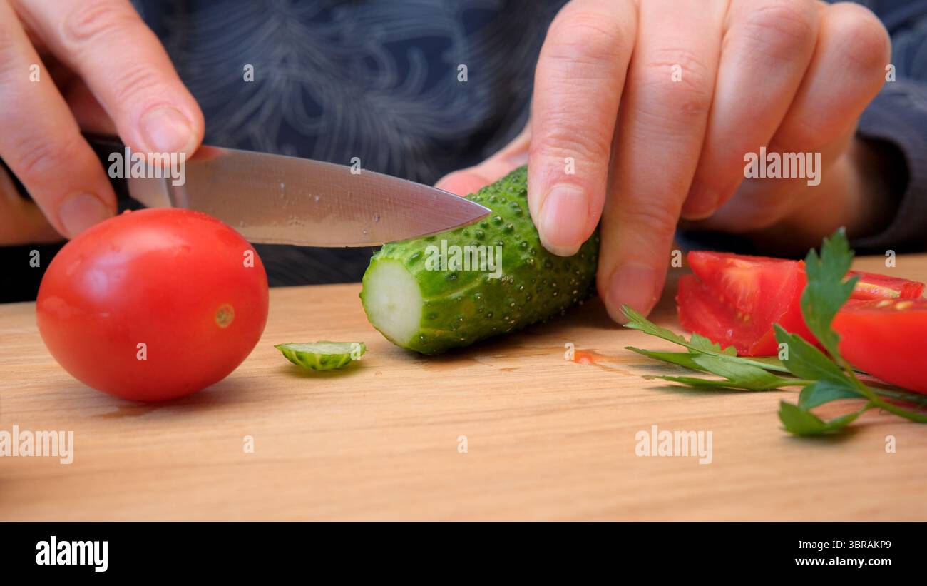 Hands slice cucumbers and tomatoes, preparing a fresh dish. Stock Photo