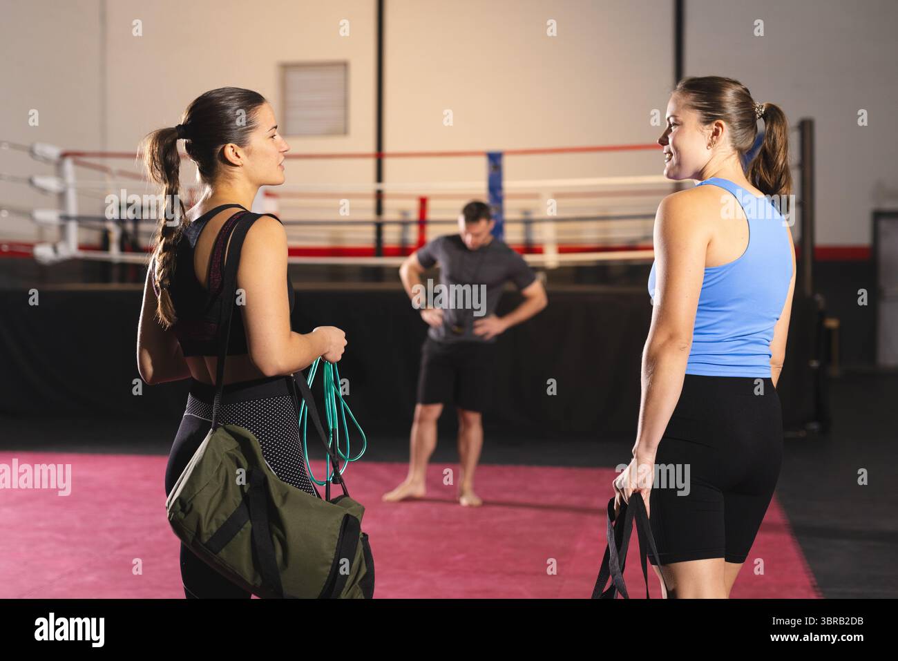Female friends training by ring ropes in boxing gym holding duffel bags ...