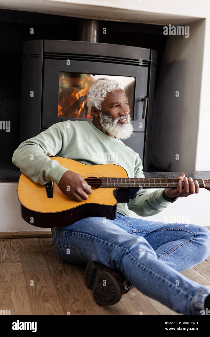 Senior African American man playing acoustic guitar sitting on floor by ...