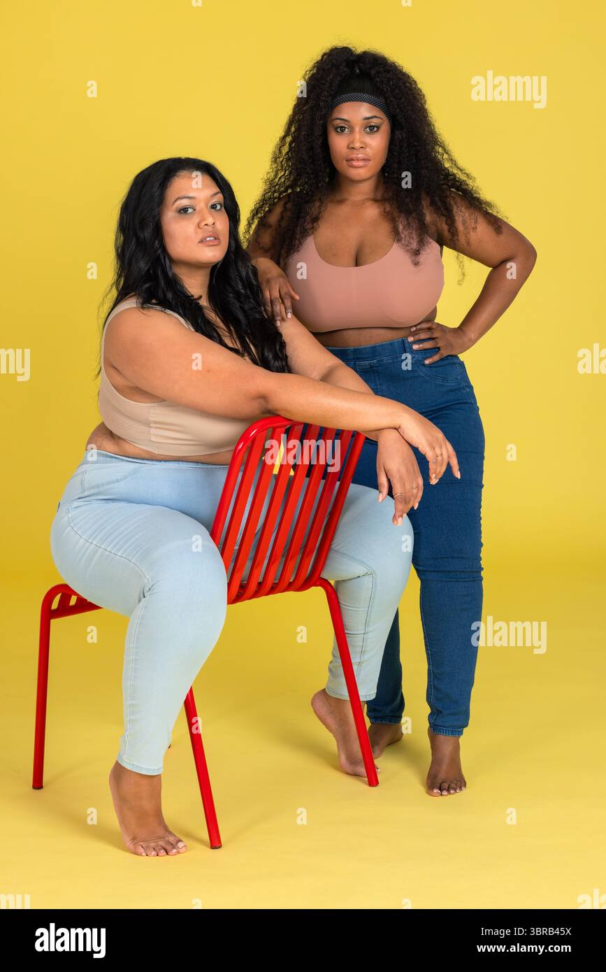 Opposing Models Diverse female models posing and leaning on red slatted metal chair ...