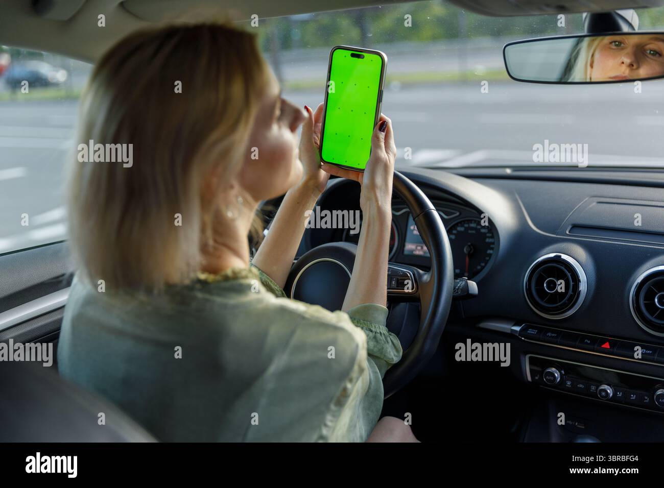 Woman in a Car Holding a Smartphone with Green Screen While Driving: A Glimpse Into Multi-tasking and Technology's Role in Modern Commuting Stock Photo