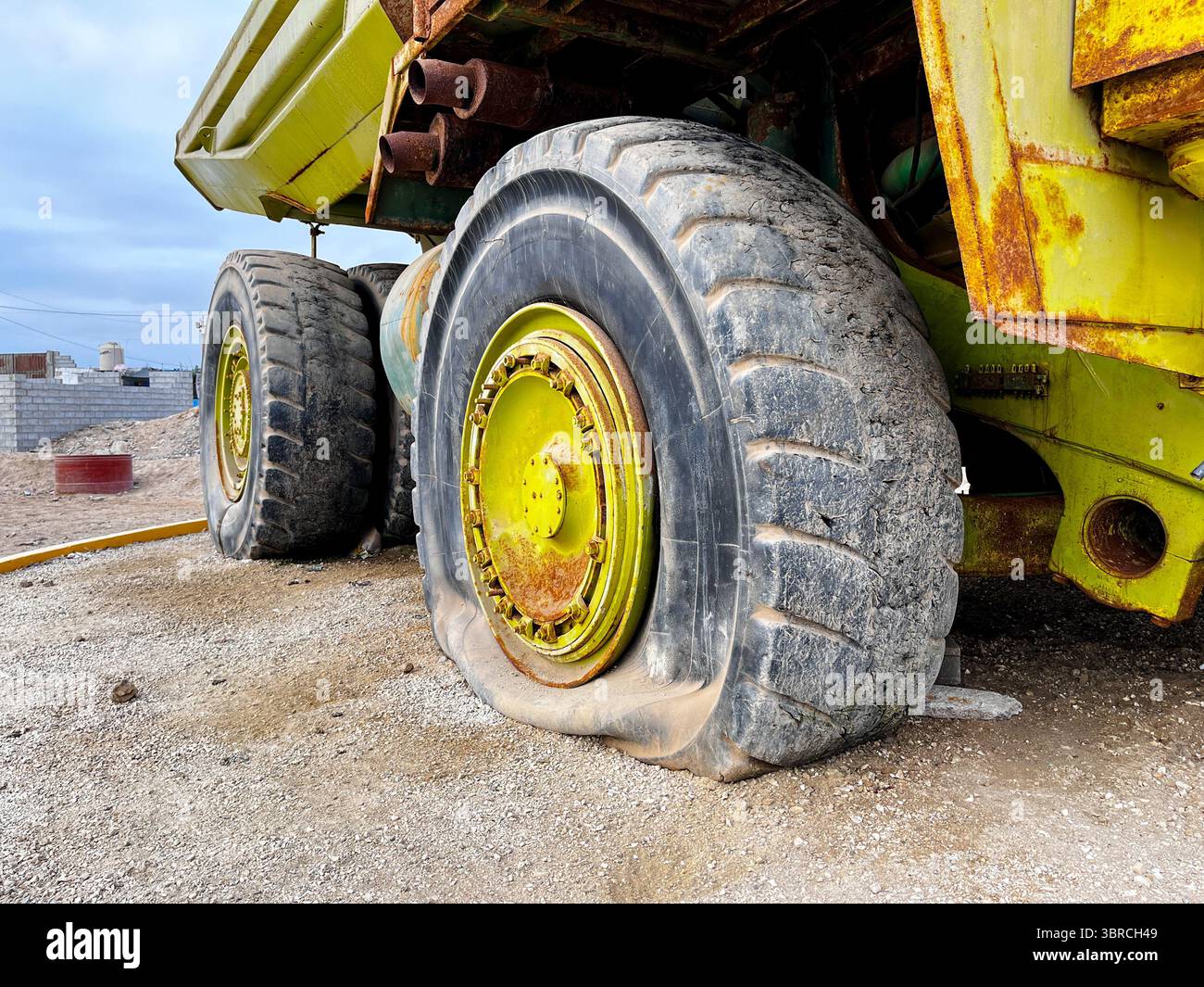 Close up of flat tire of large old quarry dump truck. Big green rusty mining truck out of work standing for exhibition on the coast of Peru Stock Photo