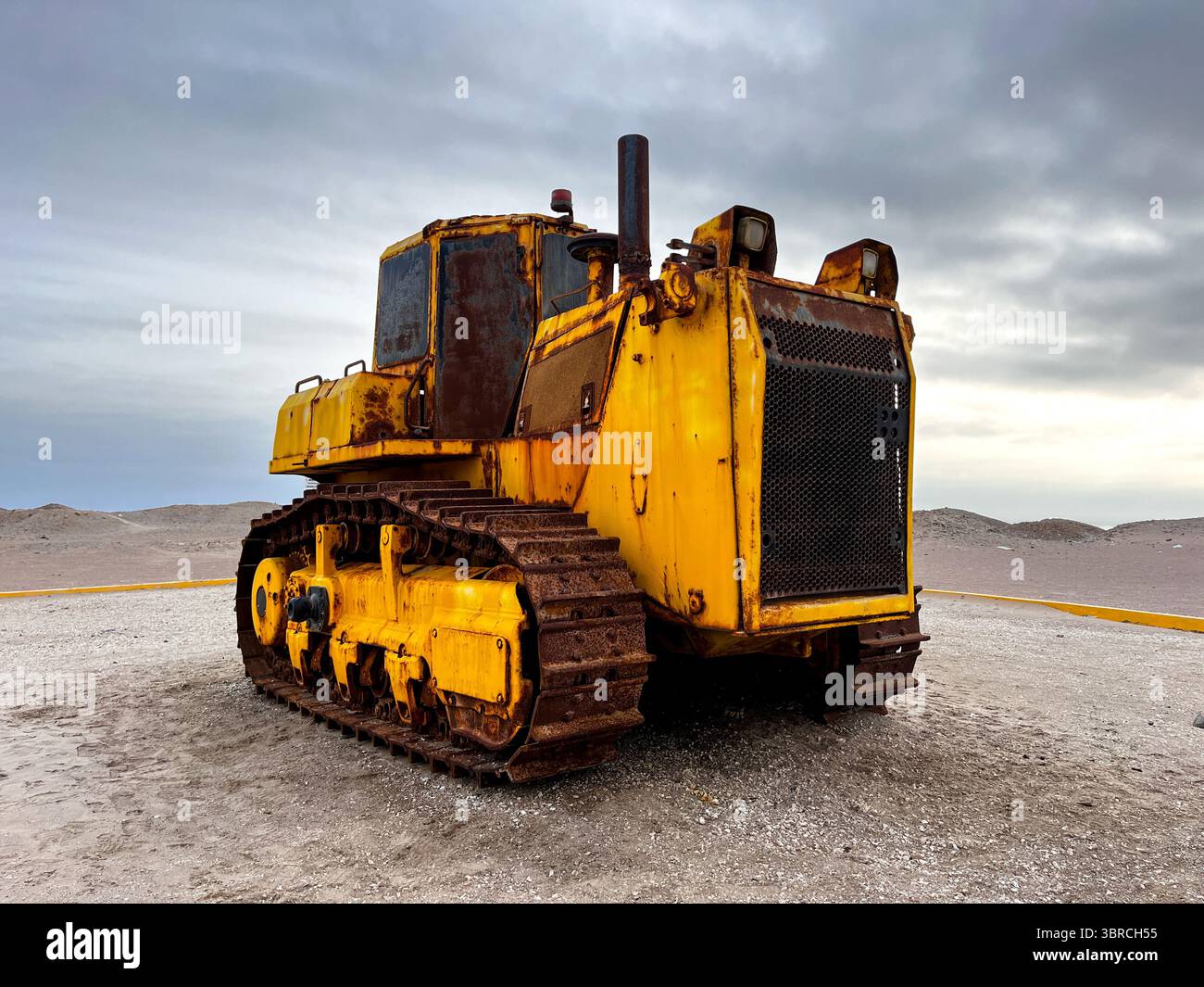 Large heavy old rusty mining vehicle out of work standing for exhibition on the coast of Peru in San Juan de Marcona with dramatic sky in background. Stock Photo