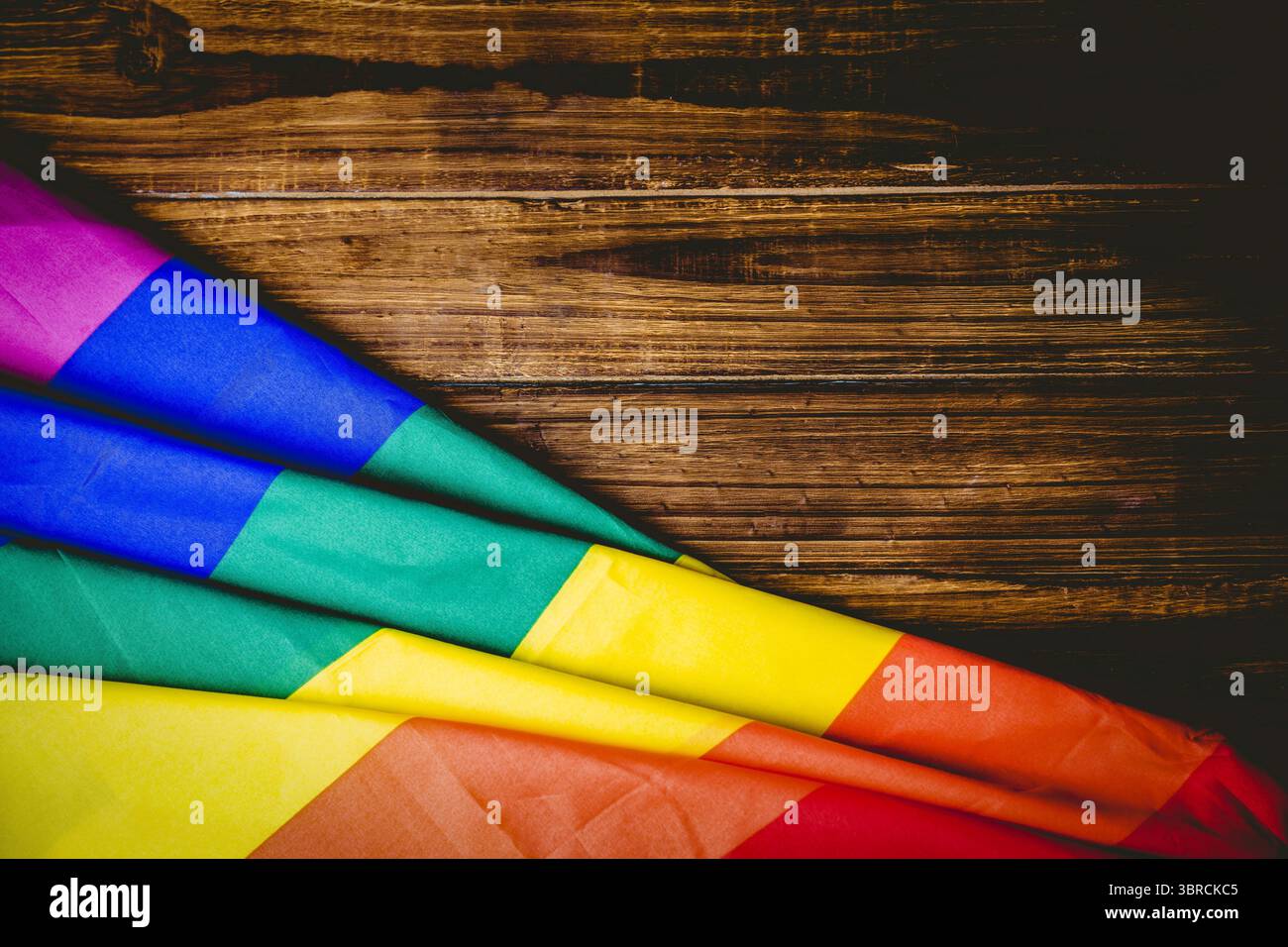 Flat design draping folded rainbow-striped flag on wood planks creating vivid contrast, copy space Stock Photo