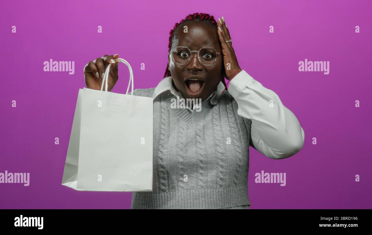 Woman expressing surprise while holding a white shopping bag against a vibrant pink background, showcasing joyful emotions and stylish appearance. Stock Photo