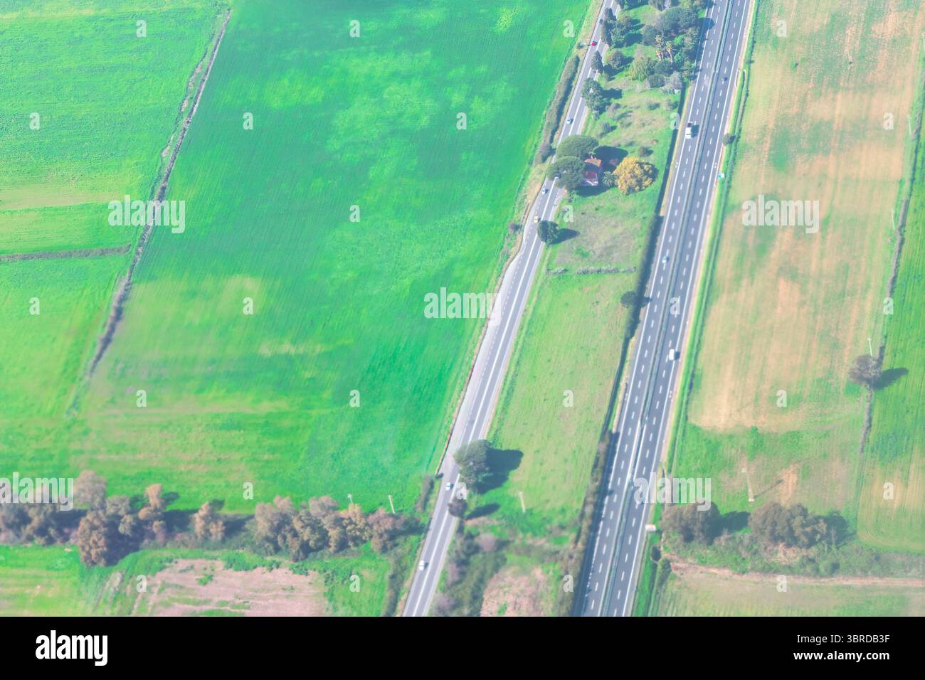 Aerial photo reveals multilane highway through patchwork of agricultural fields, with vehicles cruising in both directions. Surrounding plots exhibit Stock Photo