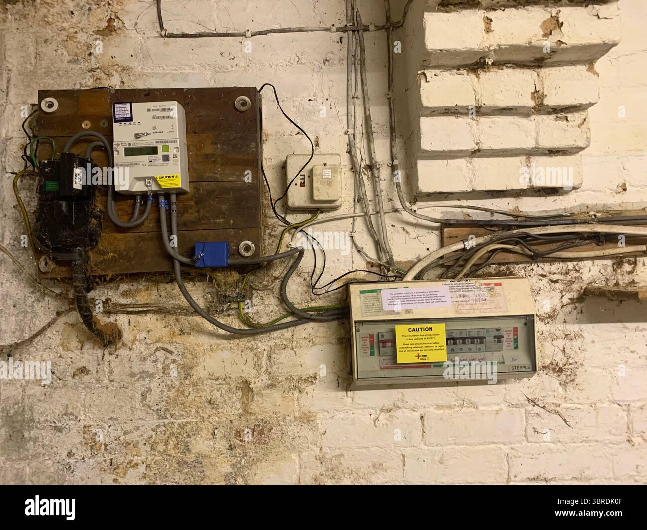 Old electrical wiring mains unit gas box pipes wires cables dirty dingy fitted to the wall in a cellar meter gas electricity wood frame electrical  UK - Smartphone Captured Stock Image