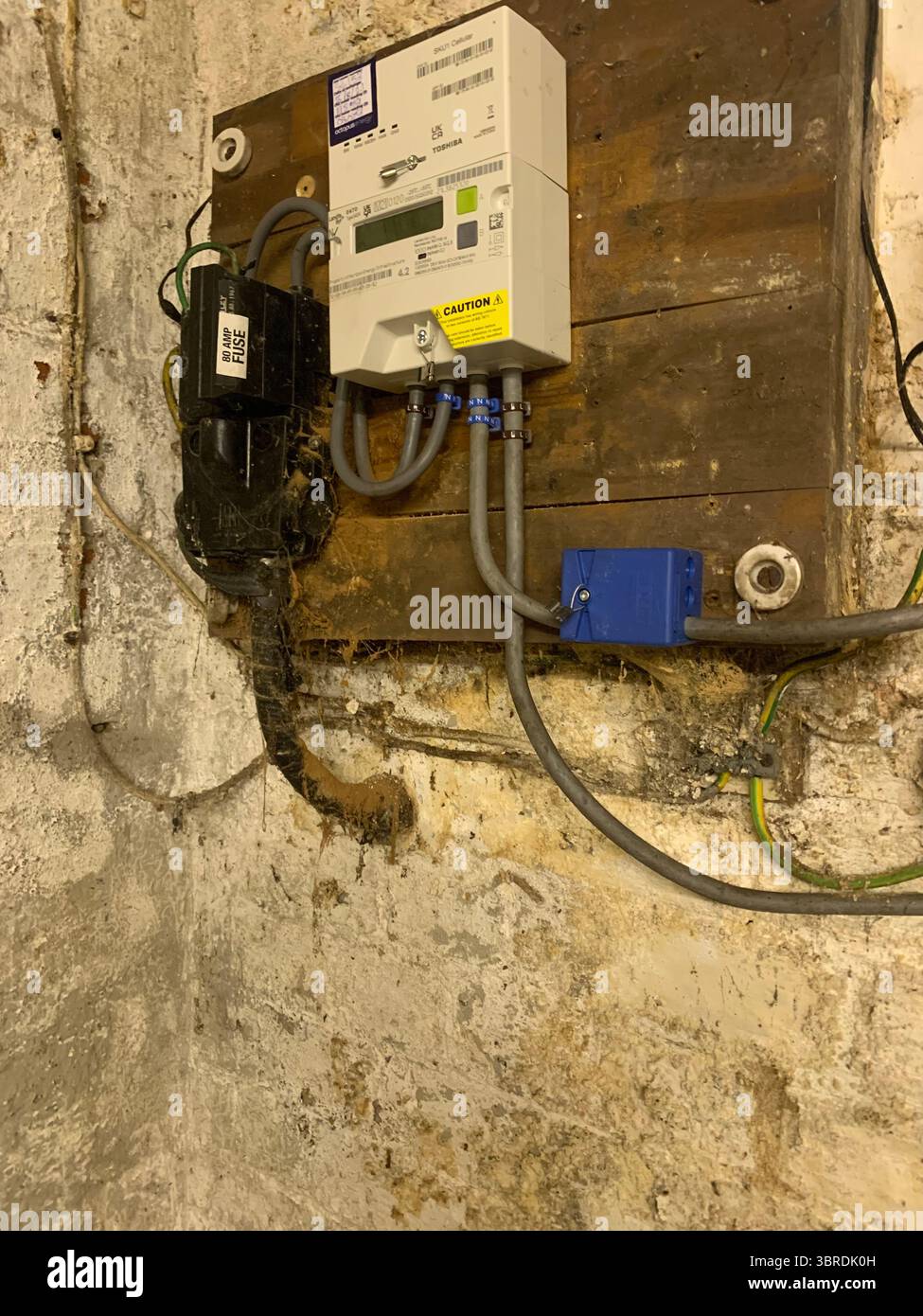 Old electrical wiring mains unit gas box pipes wires cables dirty dingy fitted to the wall in a cellar meter gas electricity wood frame electrical  UK - Smartphone Captured Stock Image