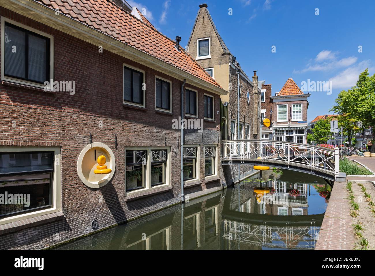 Cheese shop Gouda: A charming Dutch canal flows past historic brick houses and under a white arched bridge, capturing the essence of European charm. Stock Photo