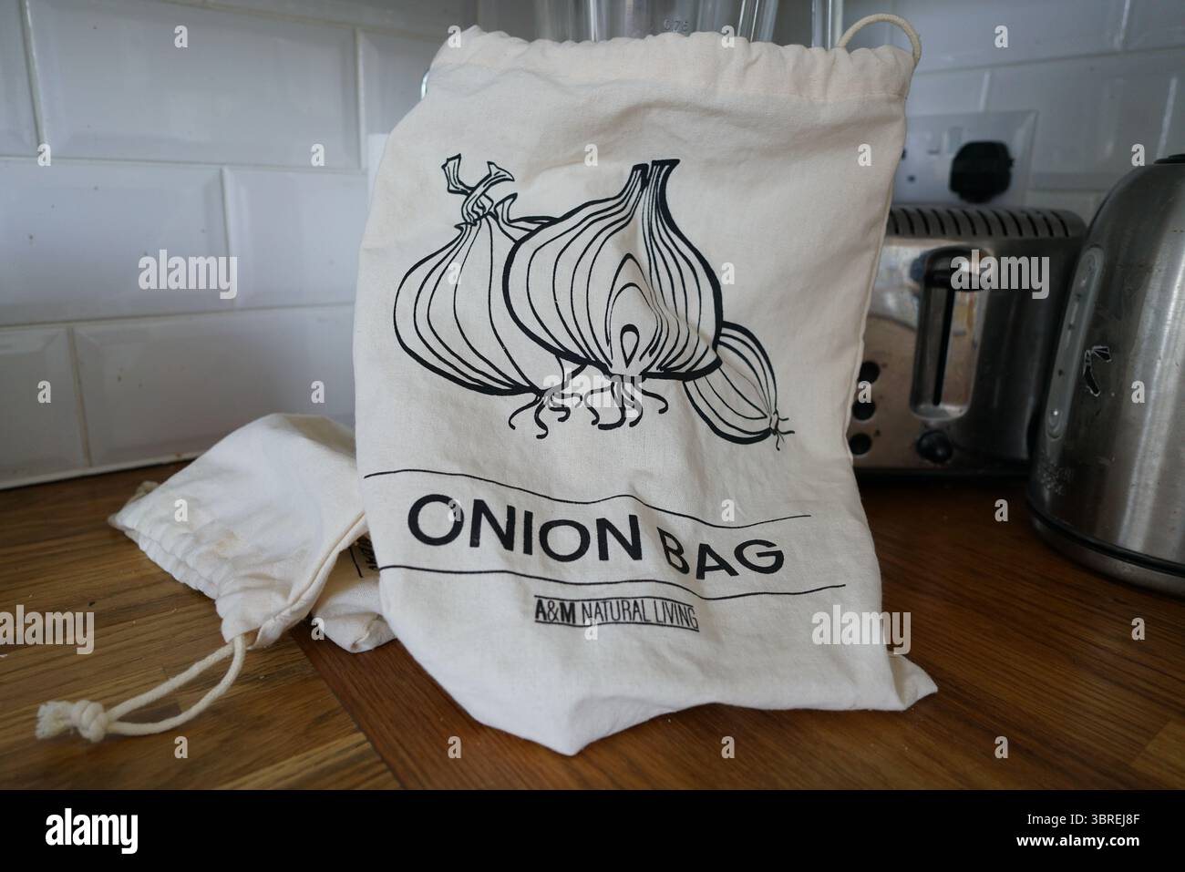 Eco-Friendly Onion Storage Bag on Wooden Kitchen Counter. Dorking, England Stock Photo