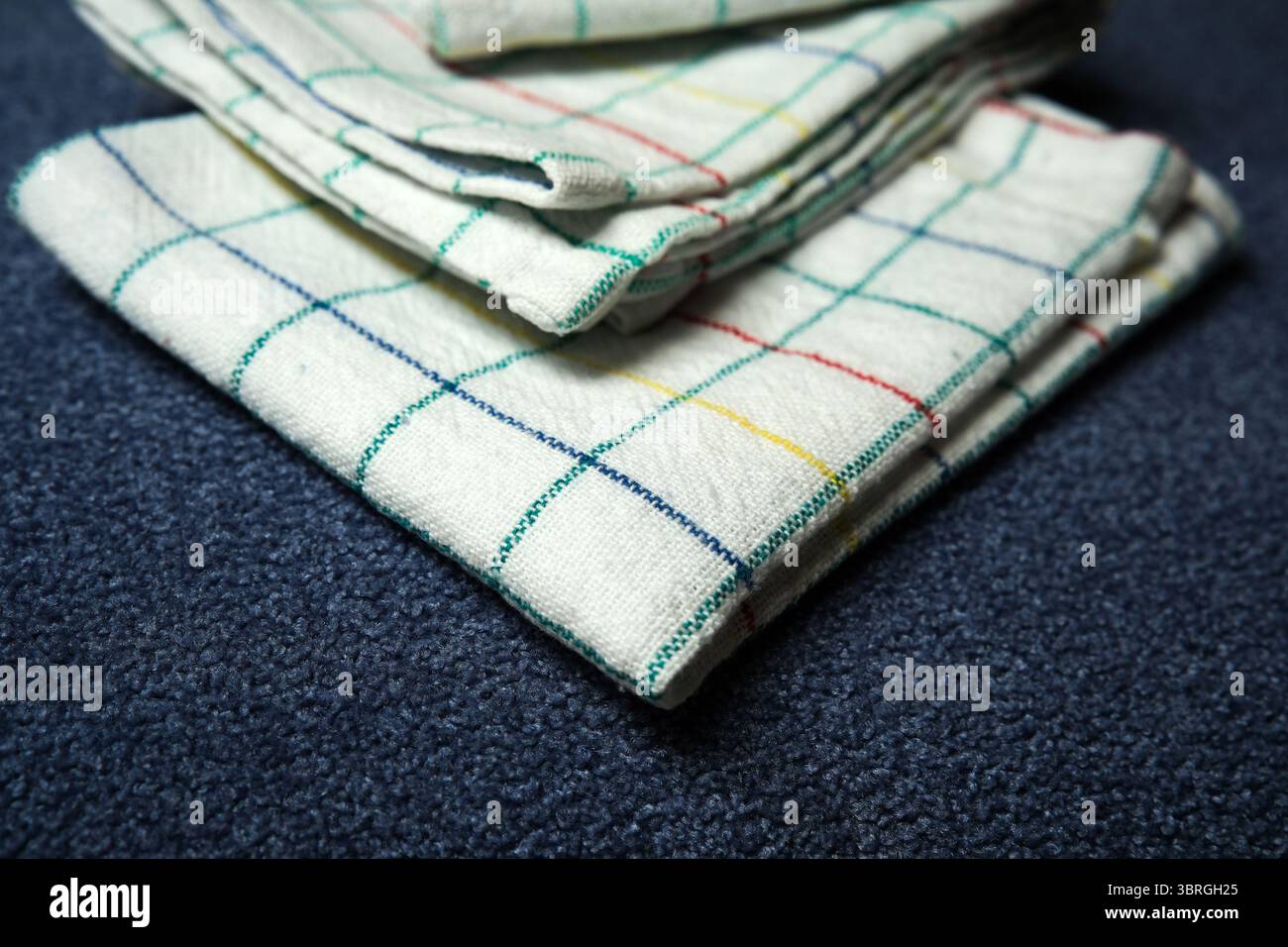 Soft checkered fabrics are neatly folded on a deep blue backdrop. Stock Photo