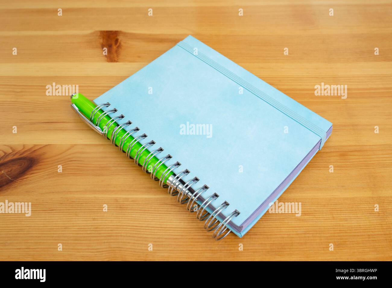 Bright blue hard cover notebook binded with a metal spring spiral on a wooden desktop Stock Photo
