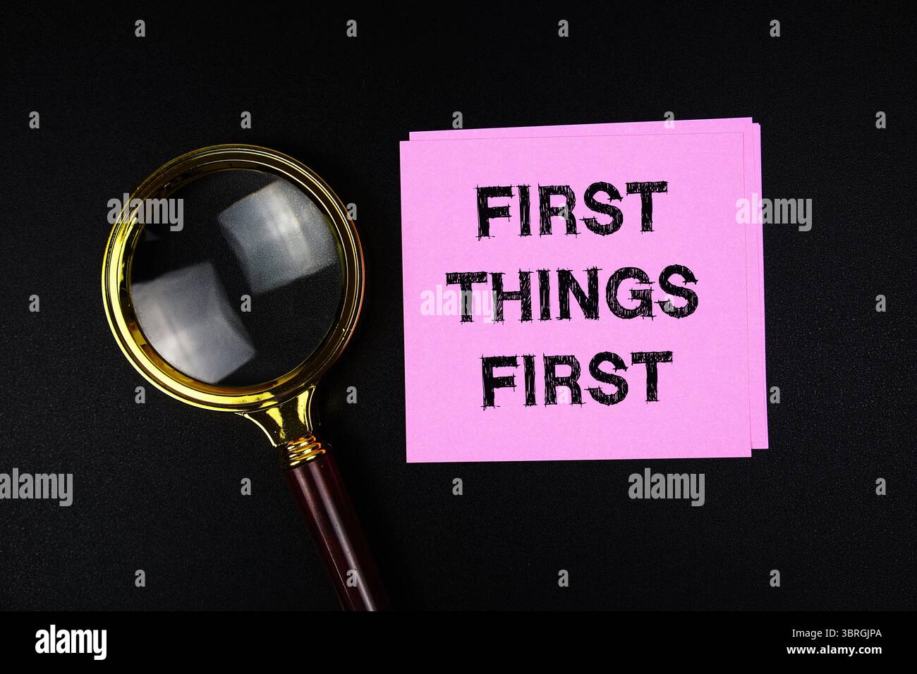 First Things First text on sticky note with magnifying glass on black ...