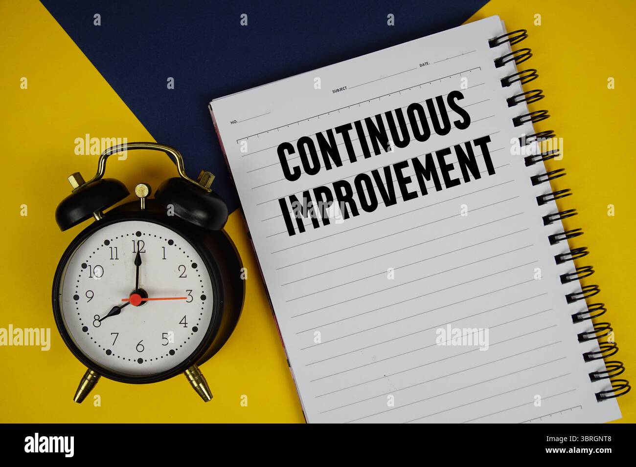 Continuous Improvement text written on notepad with alarm clock on yellow background Stock Photo