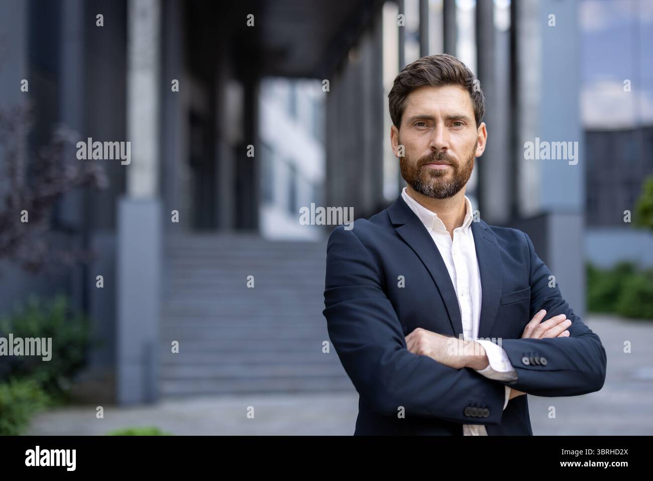 A handsome businessman in a suit stands confidently with arms crossed ...