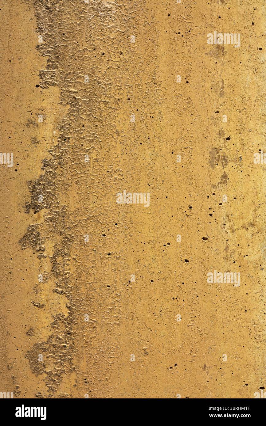 Thin paint layer on rustic concrete displays corrugated surface with scattered holes. Uneven textures create mountain like range in shades of orange. Stock Photo