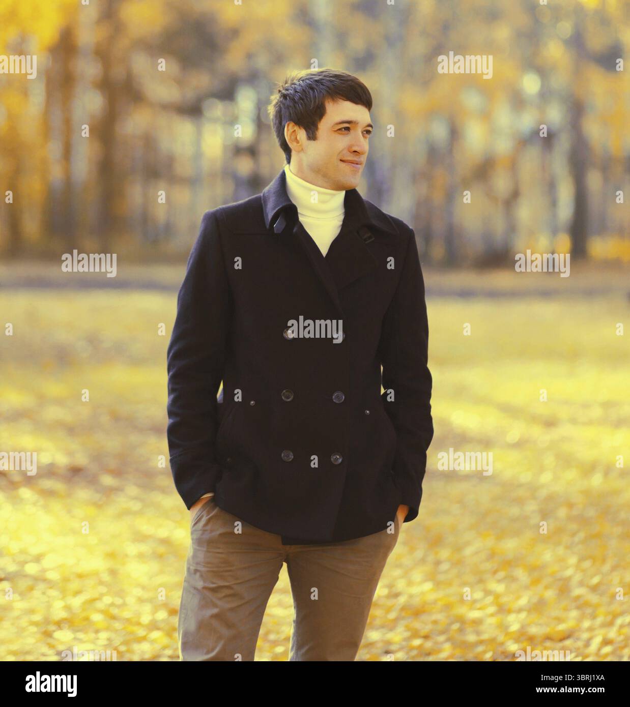 Portrait of elegant caucasian young man in black coat outdoors in autumn park with yellow leaves Stock Photo
