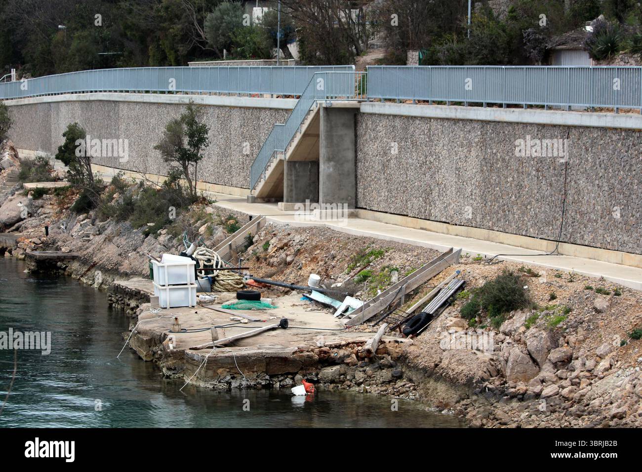 A tall concrete retaining wall with metal railing lines a coastal path ...