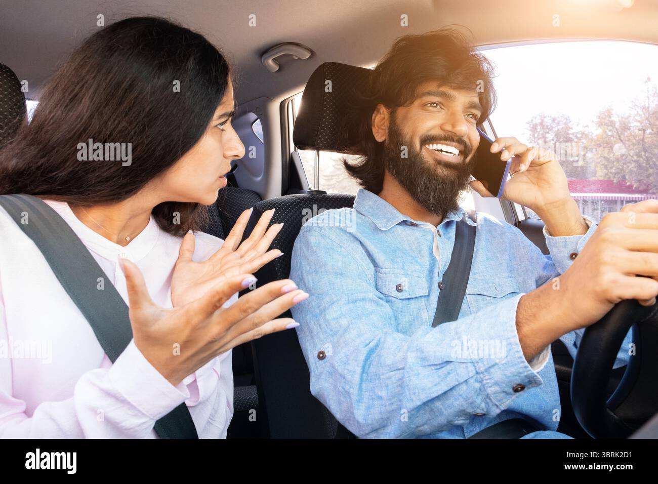 Frustrated Indian woman gesturing while man talks on phone while driving Stock Photo