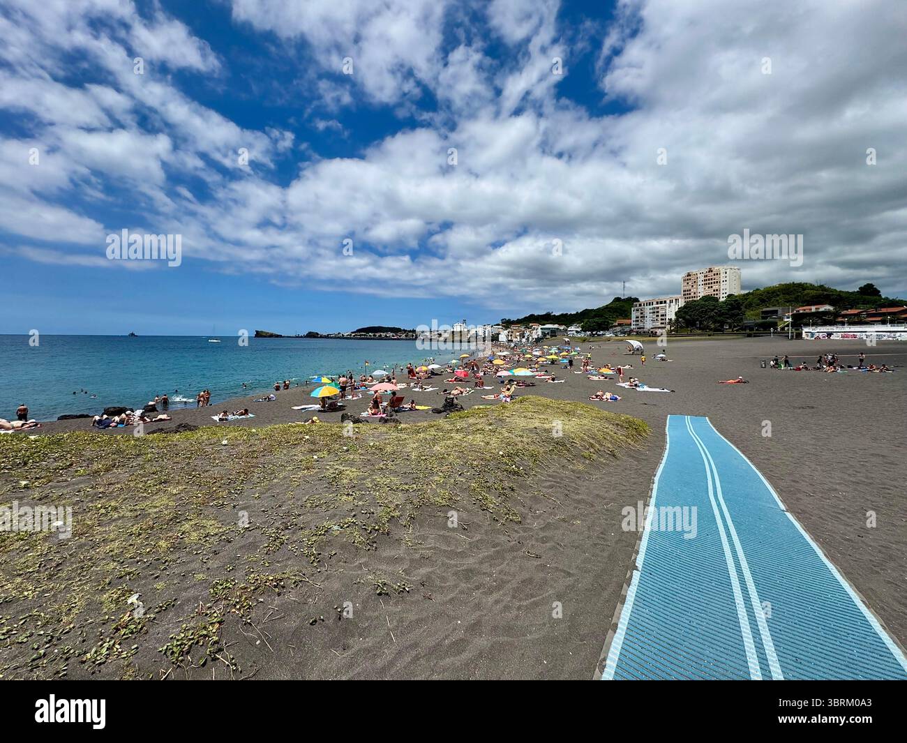 Melícias Beach with tourists relaxing on the unique black volcanic sand, located on São Miguel Island, Azores, Portugal, on a partly cloudy summer day - Smartphone Captured Stock Image