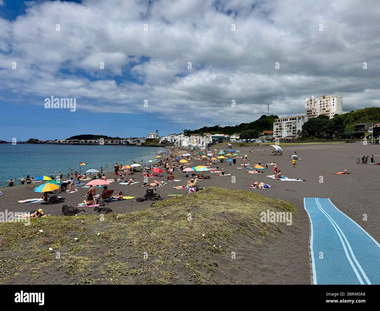Melícias Beach with tourists relaxing on the unique black volcanic sand, located on São Miguel Island, Azores, Portugal, on a partly cloudy summer day - Smartphone Captured Stock Image
