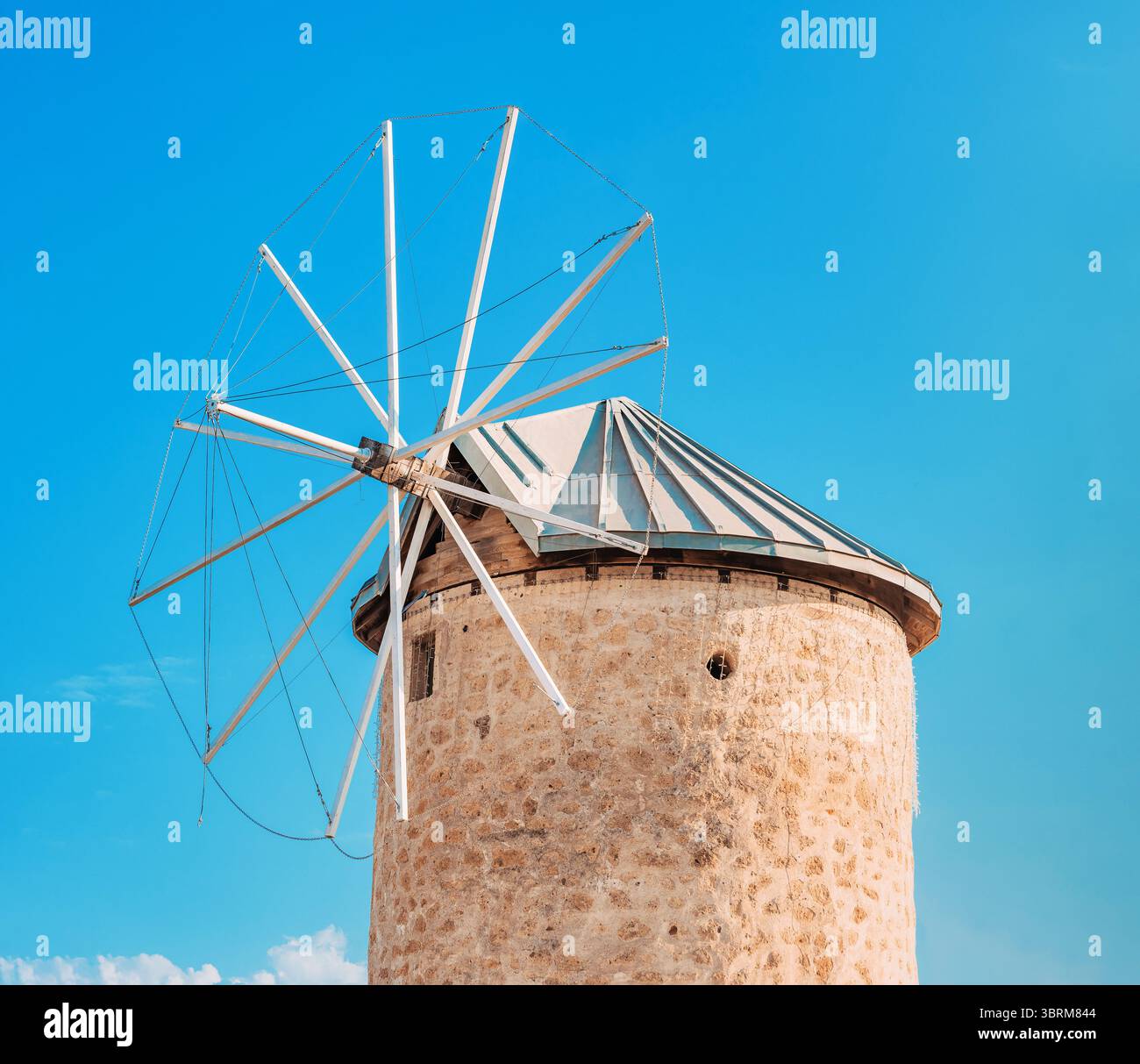 Traditional stone windmill rotating against a vibrant blue sky ...