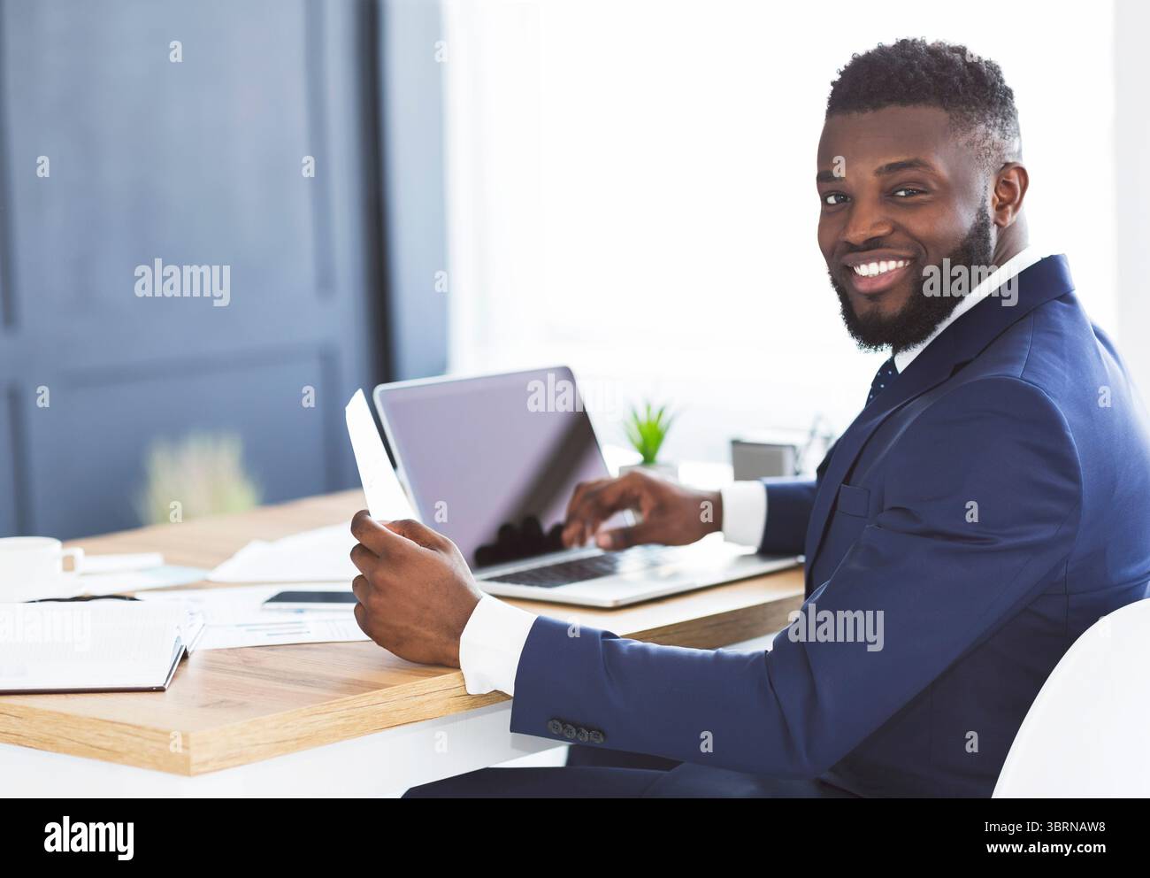 Cheerful black general manager checking reports, sitting in office Stock Photo