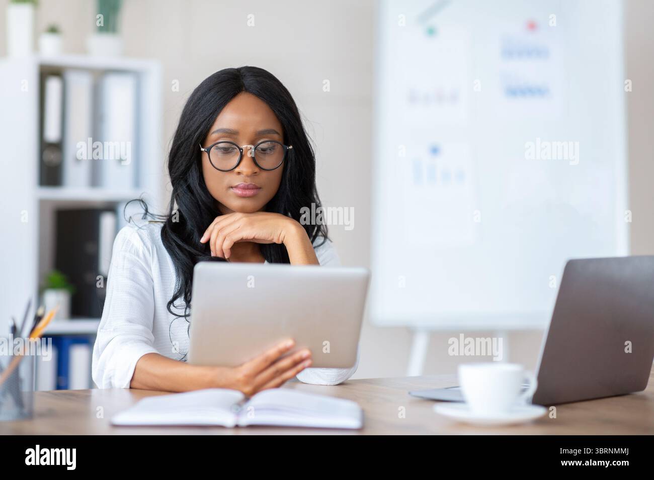 Focused young black business lady using tablet pc at her workplace in modern office, copy space Stock Photo
