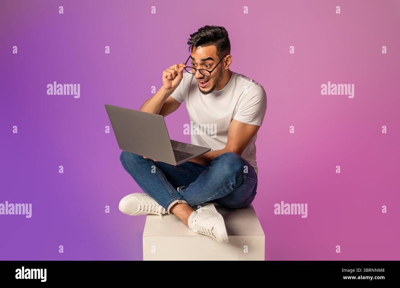 Millennial Arab man sitting cross legged with laptop pc, touching ...