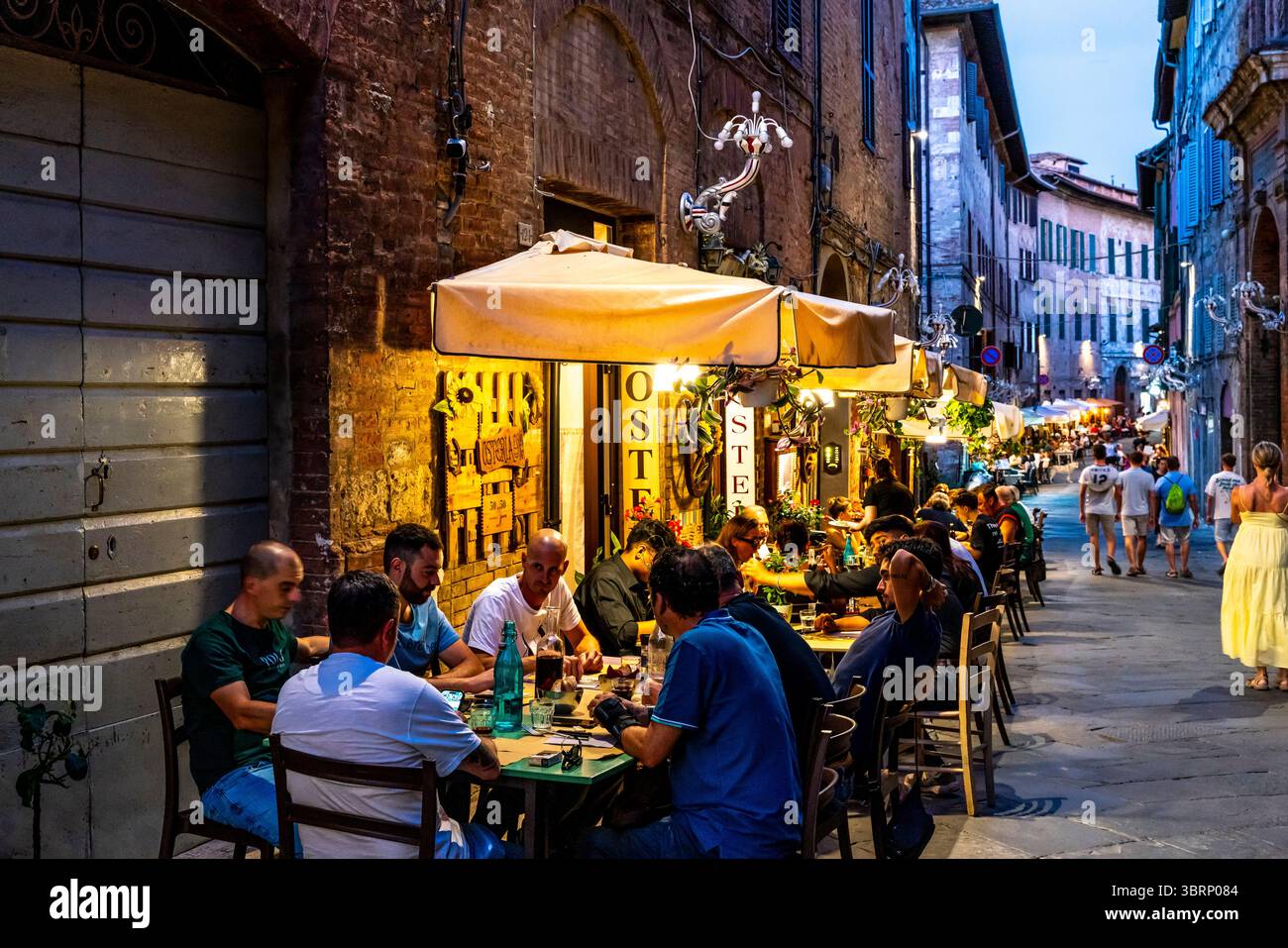 People Sitting Down Outside A Restaurant Eating Dinner In The City of Siena, Tuscany, Italy. Stock Photo