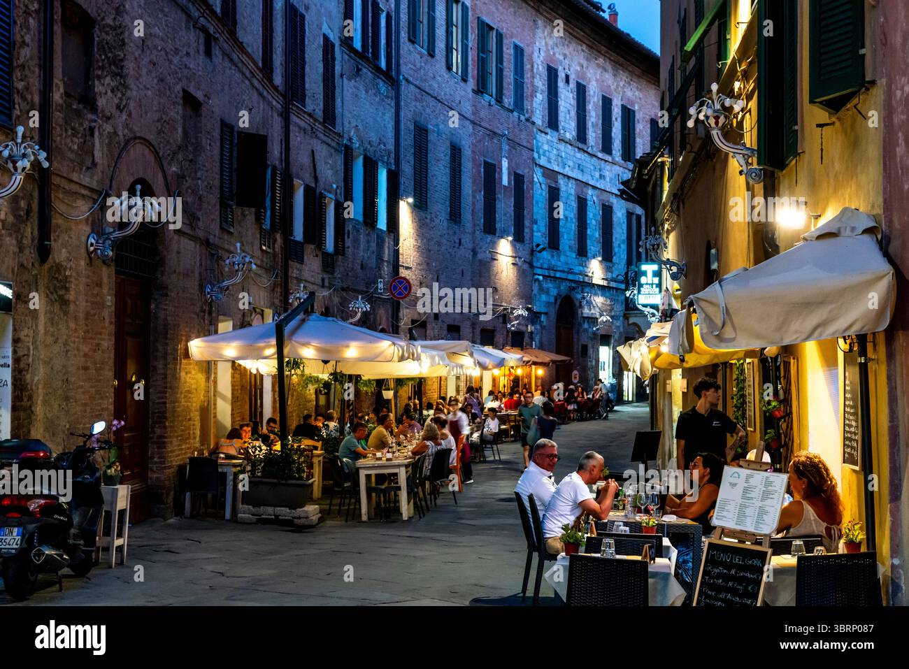 People Sitting Down Outside A Restaurant Eating Dinner In The City of Siena, Tuscany, Italy. Stock Photo