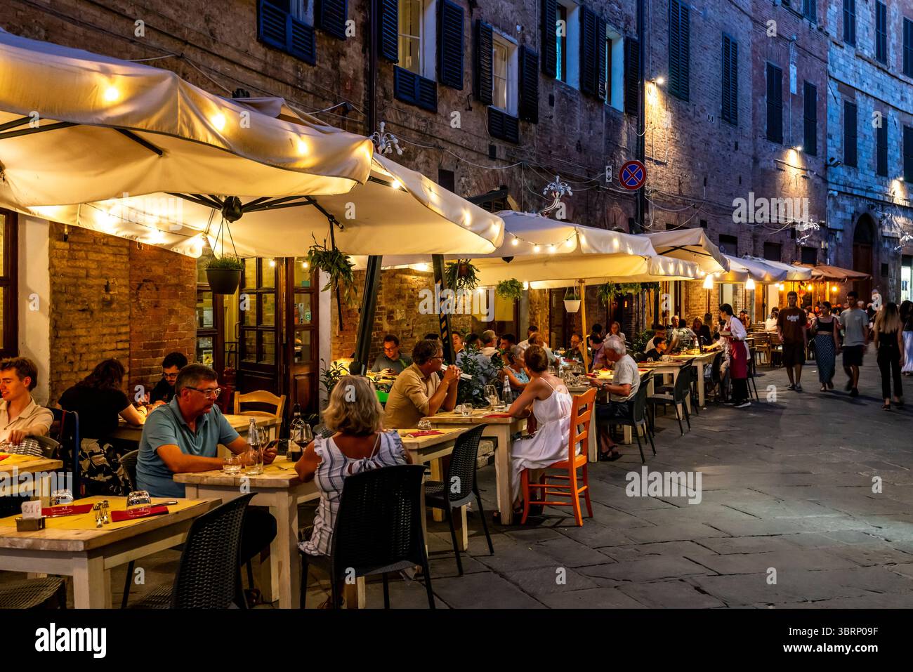 People Sitting Down Outside A Restaurant Eating Dinner In The City of Siena, Tuscany, Italy. Stock Photo