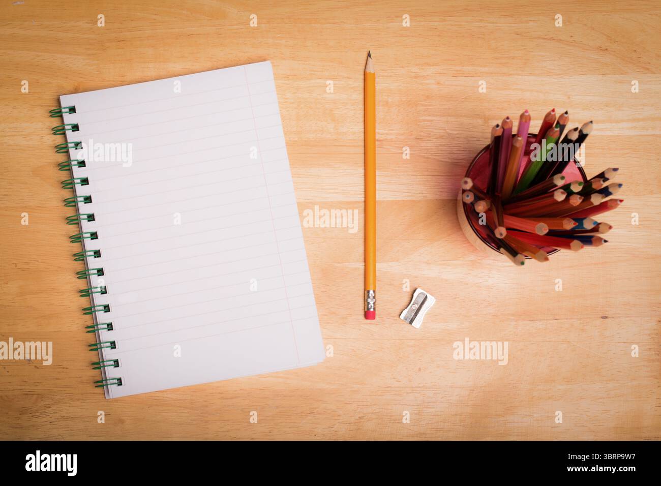 Flat top-down design showing blank spiral notebook on desk with pencil and sharpener, color pencils Stock Photo
