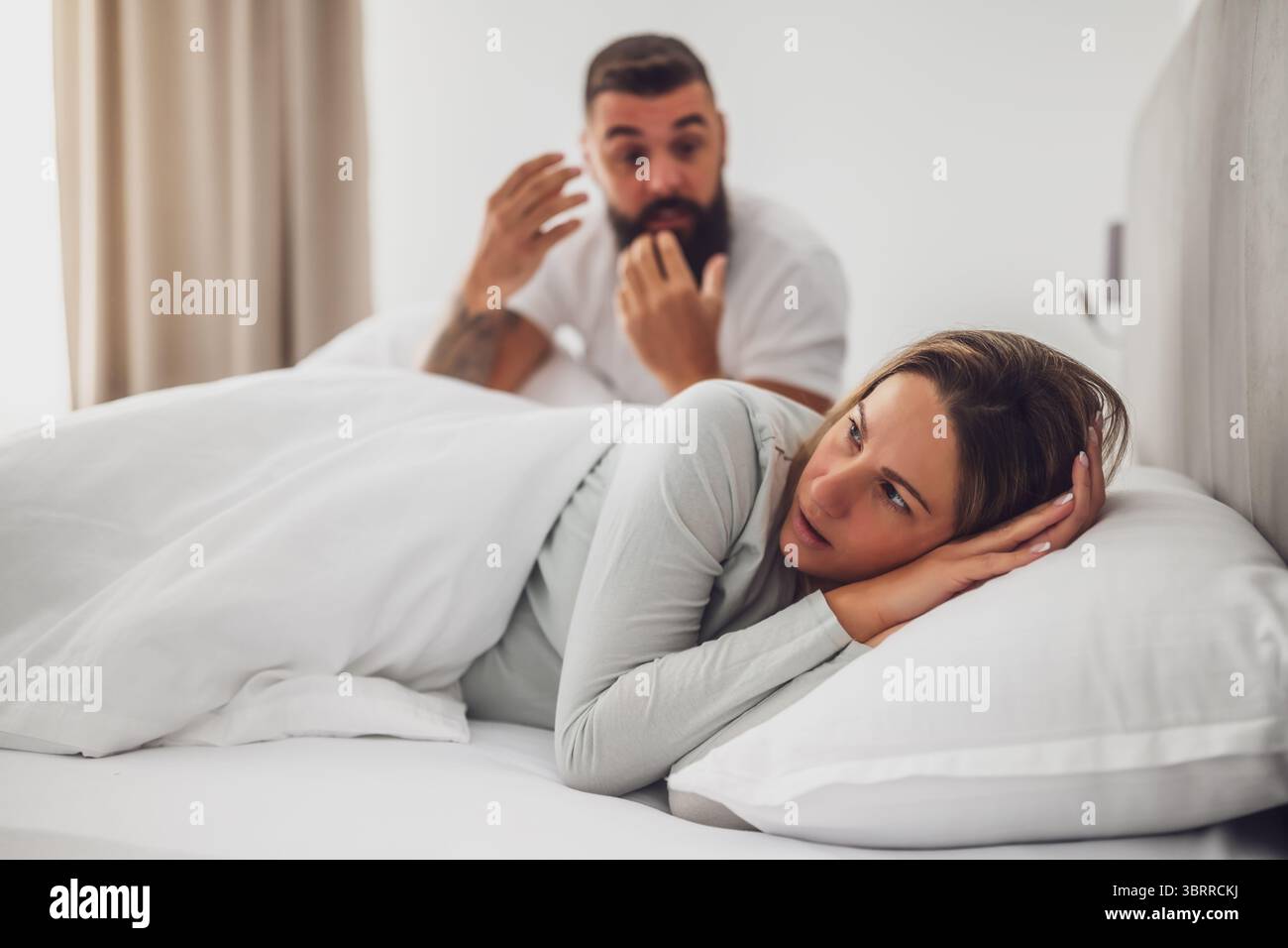 Couple is lying in bed and arguing. The woman is angry and offended and ...