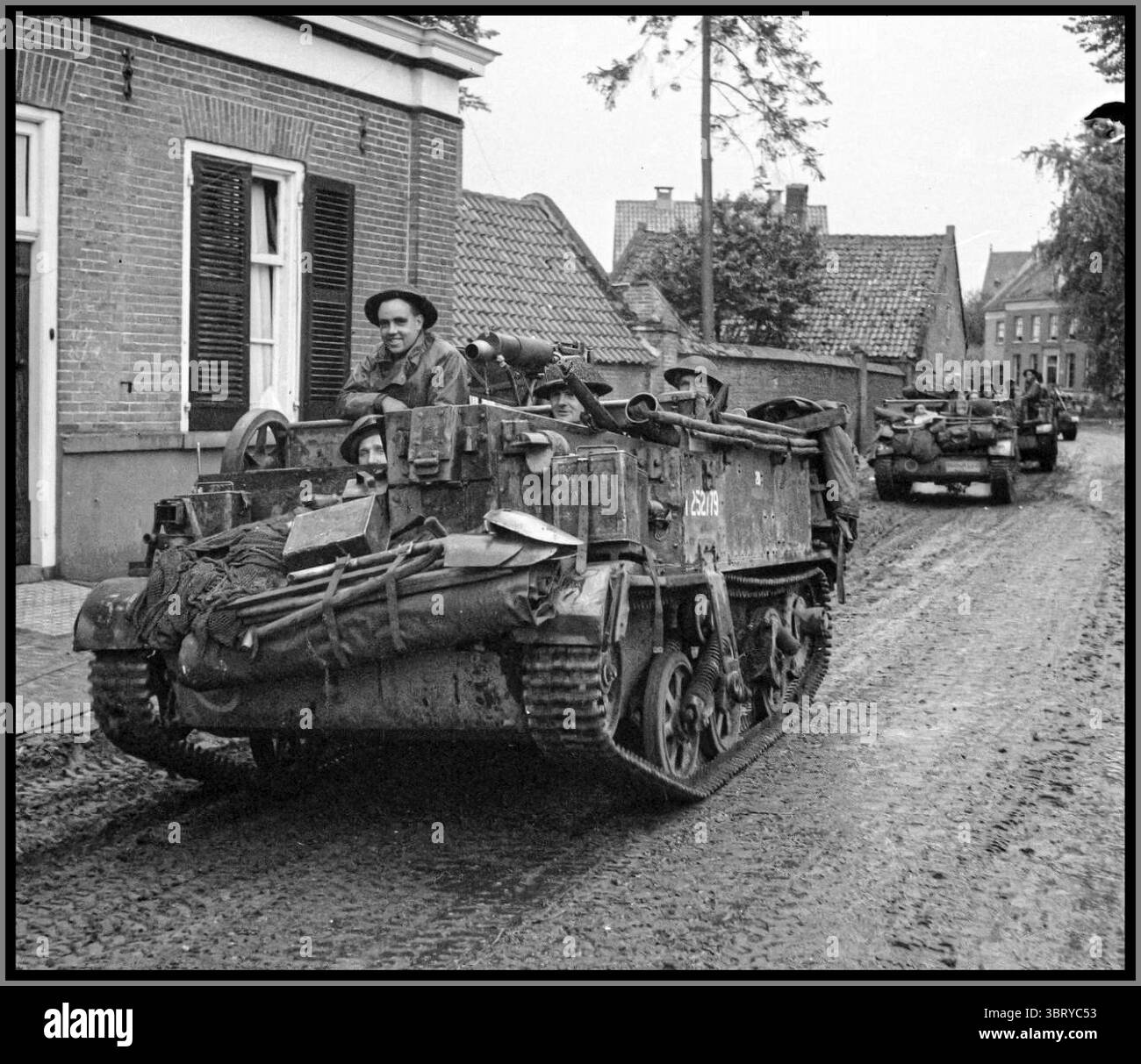 WW2 Universal Bren Carriers of the British Army in Deurne, Netherlands, during their advance towards Gemert on September 26, 1944.  Universal Carriers were lightly armored tracked vehicles widely used by Allied forces during World War II for various roles, including personnel transport, reconnaissance, and carrying machine guns or mortars.  The scene is part of the larger North-West Europe campaign, specifically during Allied advance through  Netherlands in autumn of 1944.  The photo captures a moment of wartime movement, showing soldiers on board the carrier as they navigate through a village Stock Photo
