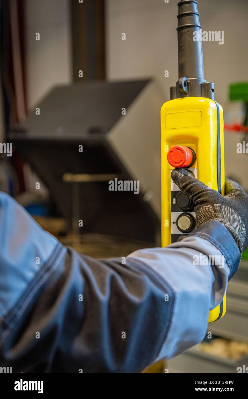 Factory worker wearing gloves using a control pendant, pushing red emergency button on yellow control panel Stock Photo