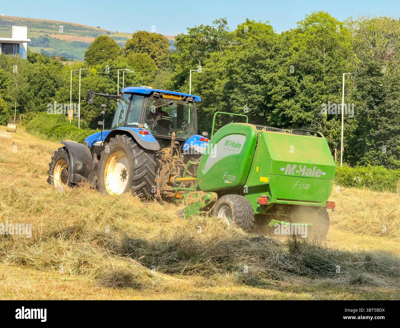 Pontypridd, Wales, UK - 12 July 2025: Tractor towing a baling machine to make large round bales from dried grass in a farm field. - Smartphone Captured Stock Image