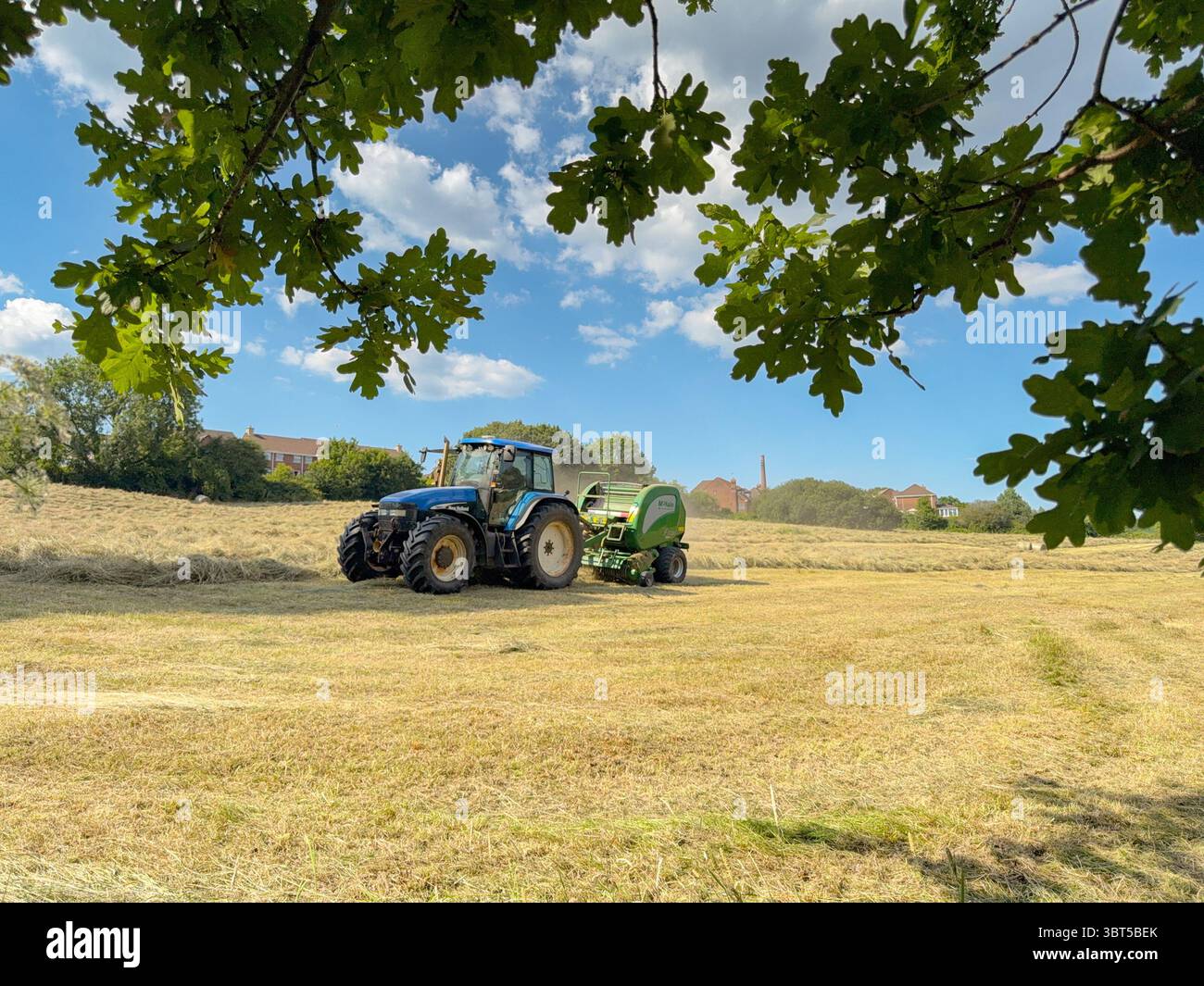 Pontypridd, Wales, UK - 12 July 2025: Tractor towing a baling machine to make large round bales from dried grass in a farm field. - Smartphone Captured Stock Image