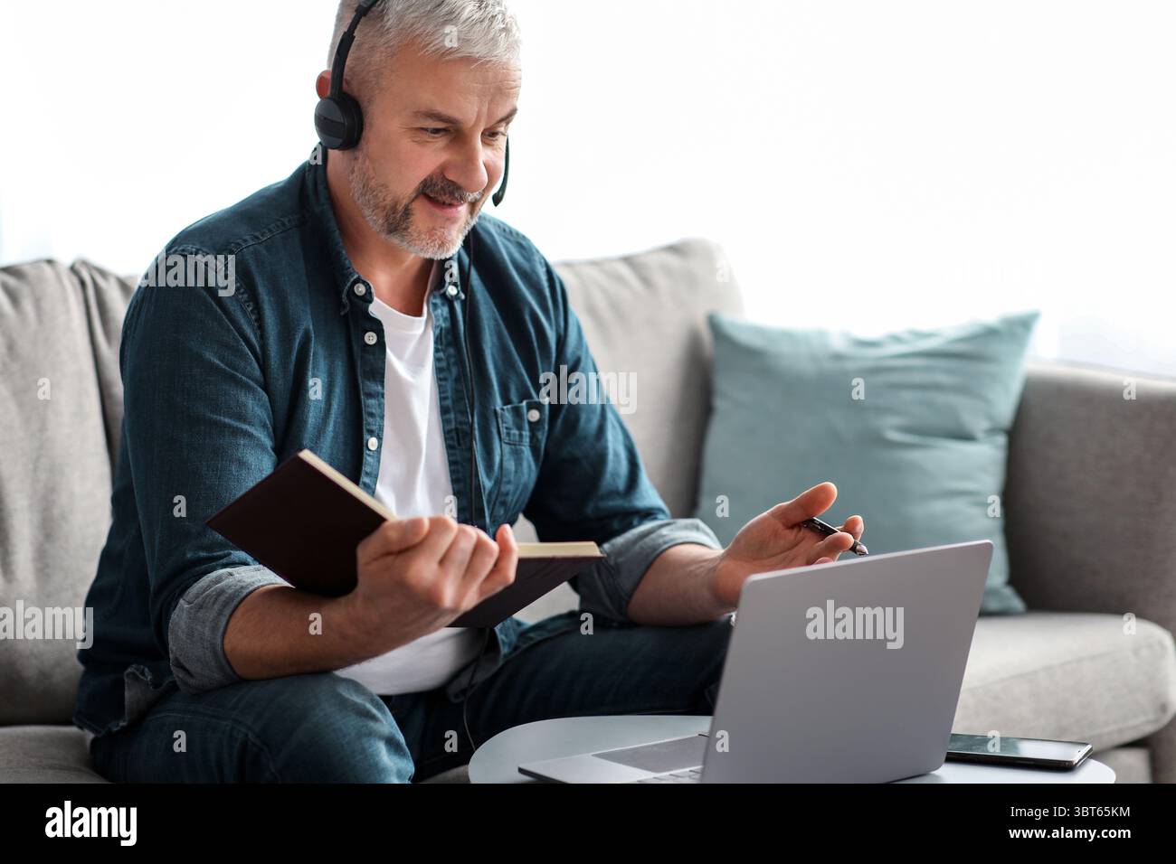 Happy old man having online class, using laptop and headset Stock Photo