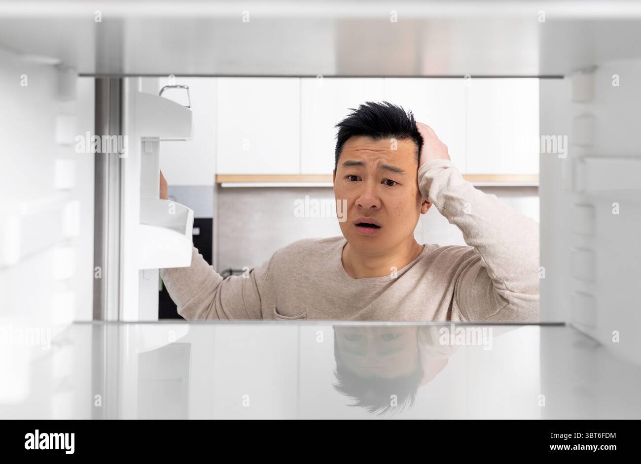 Shocked chinese man looking inside empty fridge Stock Photo