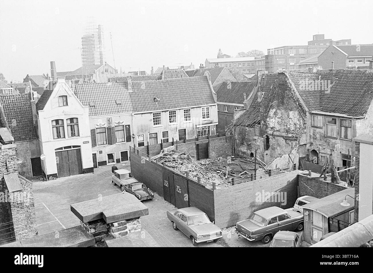 Exterior Begijnhof 20 Exterior Haarlem Begijnhof The Netherlands, Whizgle News, Dutch Desk, The Netherlands, 1950 - 2000 on 16-10-1970. These topics are shown in the image. The scene captures an urban landscape, predominantly characterized by mid-20th century architecture. Various buildings with distinct features such as steeply pitched roofs and brick façades are present. The structures appear aged, with some exhibiting signs of wear and neglect, such as peeling paint and crumbling walls, particularly evident in the building on the right with its exposed brick and scattered debris. In the for Stock Photo