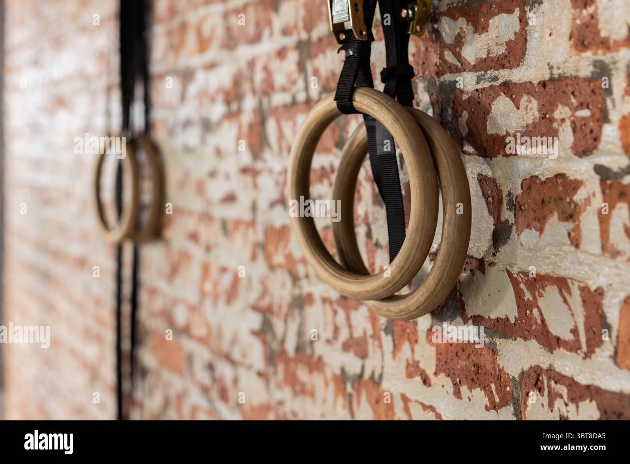 Wooden gymnastic rings hanging from black straps on exposed brick wall inside fitness studio Stock Photo