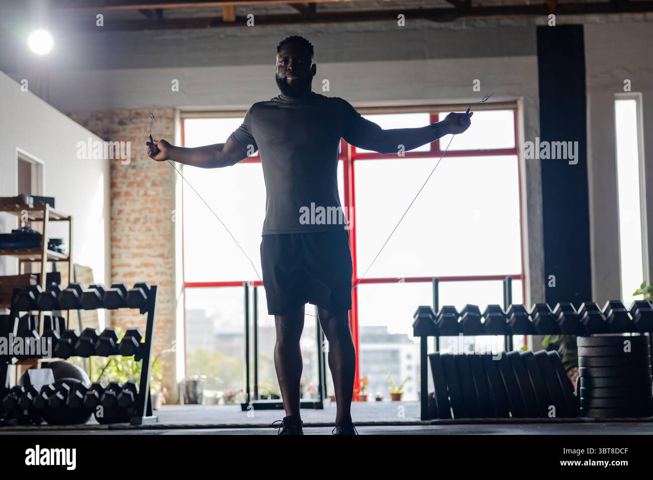 African American man in late twenties skipping rope in converted warehouse gym wearing sportswear Stock Photo
