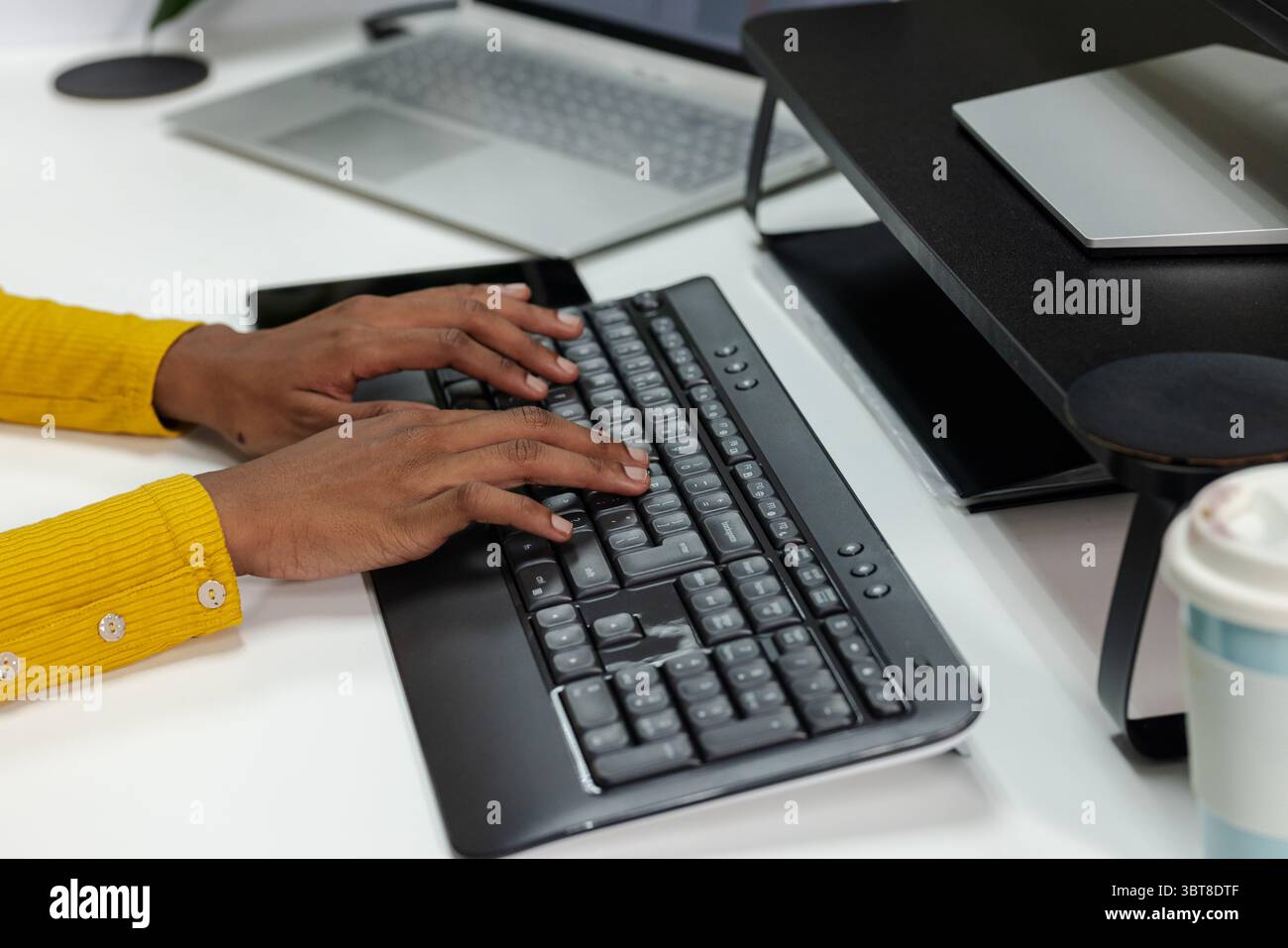 African American man sitting at white desk in home office typing on black wireless keyboard Stock Photo