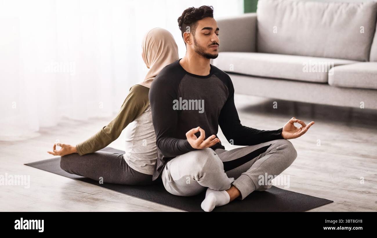 Young Middle Eastern Spouses Meditating Together On Mat In Living Room Stock Photo