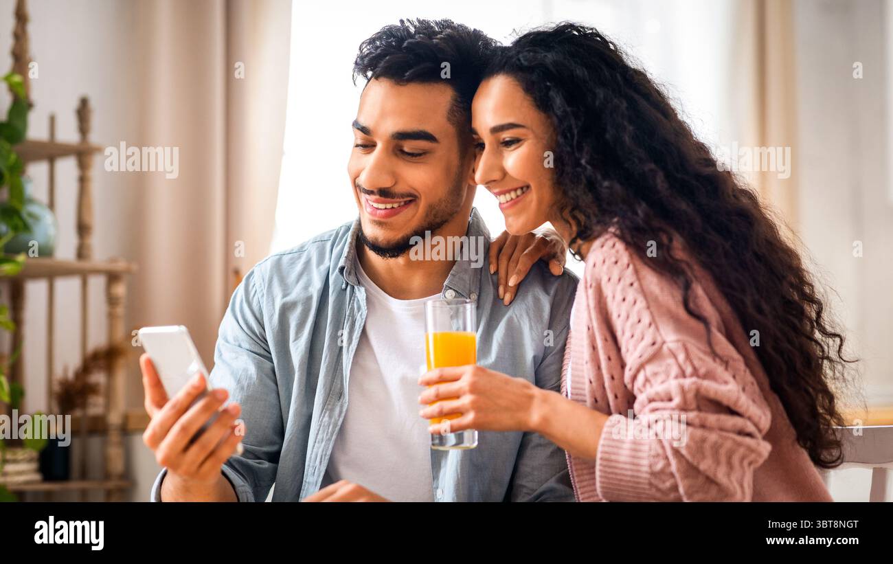Happy Middle Eastern Couple Browsing Internet On Smartphone While Having Breakfast Stock Photo