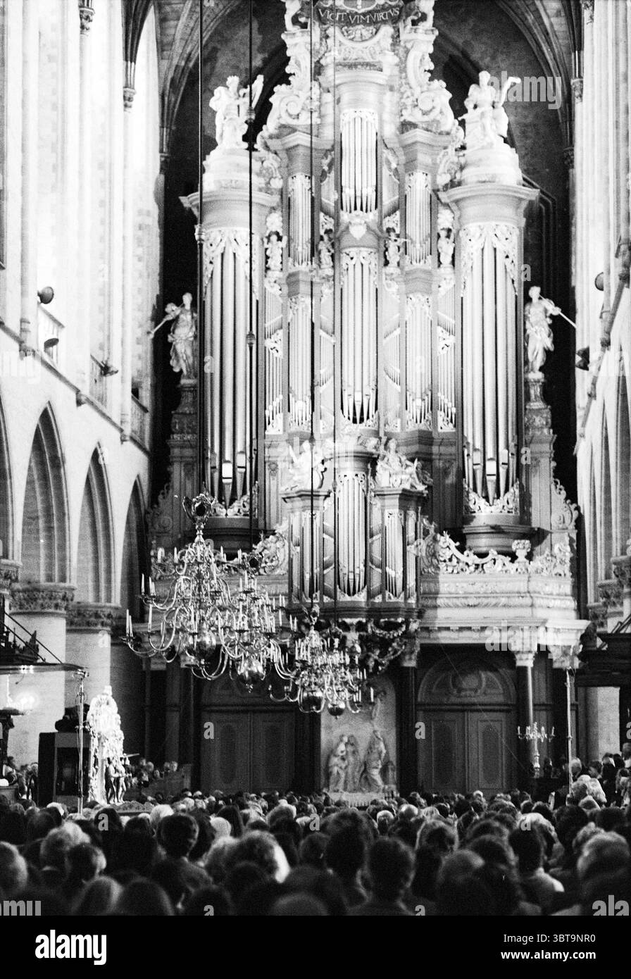 Organ month: barrel organs in Gr. Church barrel organs, Whizgle News, Dutch Desk, The Netherlands, 1950 - 2000 on 10-07-1979. The image contains these topics. The scene is set within a grand, expansive interior, likely a cathedral or historical church, characterized by towering ceilings that create an atmosphere of grandeur. The walls are adorned with intricate stonework, featuring arches and vertical columns that draw the eye upward, enhancing the sense of height. Dominating the background is a magnificent organ, its multiple pipes gleaming in the soft light. Elaborate carvings, possibly depi Stock Photo