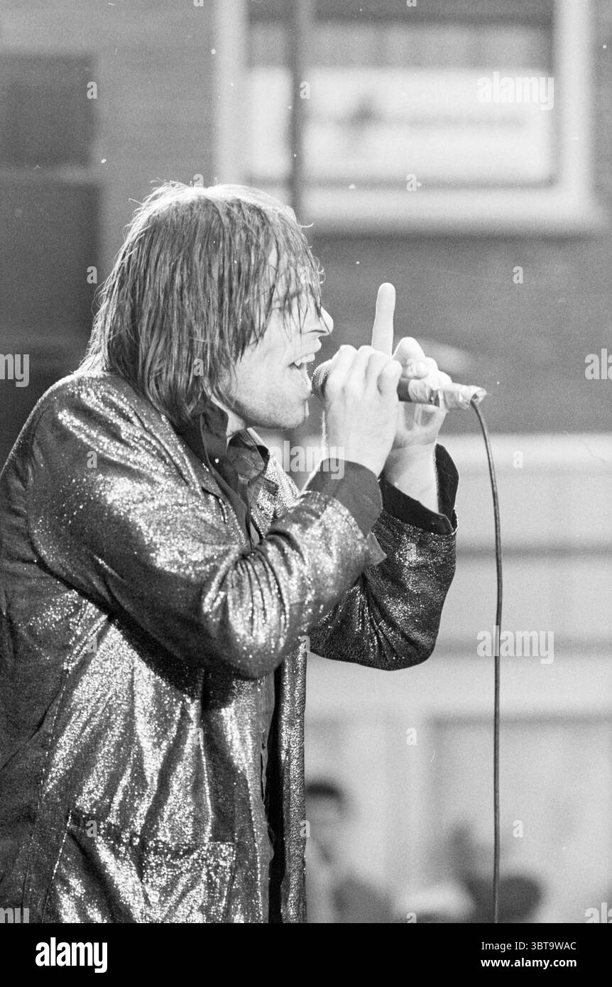 Liberation pop butter market Music Haarlem Botermarkt The Netherlands, Whizgle News, Dutch Desk, The Netherlands, 1950 - 2000 on 05-05-1987. These are the elements in the image. The scene features a captivating performance under a dimly-lit atmosphere, where a male vocalist takes center stage. He is dressed in a shiny, sequined jacket that catches the light with every movement, enhancing the energy of the moment. The jacket is predominantly black with flecks of silver and reflects light dramatically, creating a contrast against the darker elements of the background. The vocalist's hair is long Stock Photo