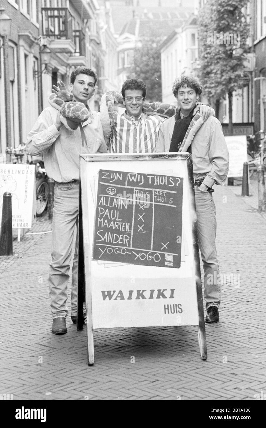 Three students in the Schagchelstraat Haarlem Schagchelstraat The Netherlands, Whizgle News, Dutch Desk, The Netherlands, 1950 - 2000 on 19-10-1992. These topics appear in the image. In a bustling street scene, three young men stand together, exuding confidence and camaraderie. The setting features narrow cobblestone streets lined with charming buildings, each adorned with decorative facades and greenery spilling from window boxes. The ambiance reflects a lively urban atmosphere. The first individual on the left holds a round object, possibly a ball, and wears a casual, light-colored shirt, pa Stock Photo
