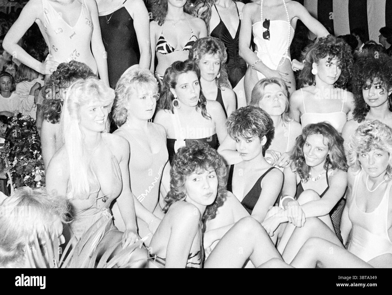 Election Miss Ijmond Miss election, Whizgle News, Dutch Desk, The Netherlands, 1950 - 2000 on 10-08-1985. These are the elements in the image. The scene is bustling with a group of women, all gathered closely together, creating a dynamic and energetic atmosphere. They are dressed in a variety of swimsuits that reflect a playful yet bold sense of style, with some opting for classic designs, while others showcase more adventurous cuts and patterns. The colors range from vibrant hues to more subdued shades, enhancing the diversity of their outfits. Their hairstyles vary significantly, ranging fro Stock Photo